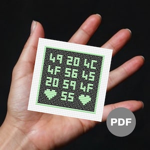 Könnte beinhalten: Ein schwarzes und grünes Kreuzstichmuster mit einem digitalen Display, das die Zahlen 49, 20, 4C, 4F, 56, 4C, 20, 59, 4F und 55 anzeigt. Zwei grüne Herzen werden in der unteren Reihe angezeigt.