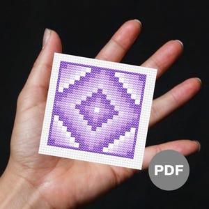 May include: A purple and white cross stitch pattern with a geometric design. The pattern is on a white background and is framed with a white border. The pattern is in a hand.
