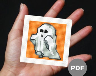 Puede incluir: Un patrón de punto de cruz con un fantasma blanco sobre un fondo naranja. El patrón está impreso en papel blanco y etiquetado como "PDF".