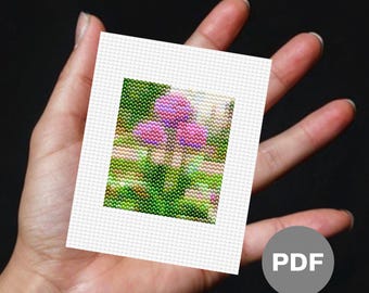 May include: A close-up of a cross-stitch pattern featuring a pink flower with green leaves.