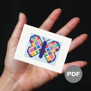 May include: A colorful butterfly cross stitch pattern with a blue background. The pattern is on a white card with the word "PDF" in a gray circle.
