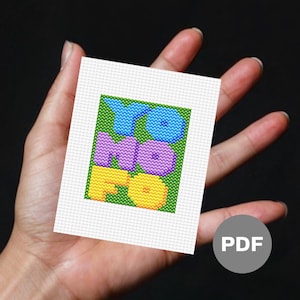 May include: A cross-stitch pattern featuring the word "YOMO" in colorful, bubble-like letters on a green background. The pattern is printed on white paper and is labeled "PDF".