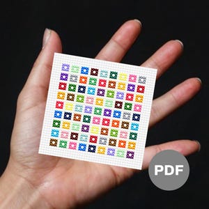May include: A small, square cross-stitch pattern featuring a grid of colorful squares. Each square is a different color, including red, blue, green, and yellow. The pattern is held in a hand against a dark background. A PDF icon is in the lower right corner.
