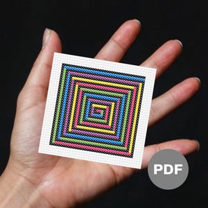 May include: A small, square cross-stitch pattern featuring concentric squares in vibrant colors: blue, green, yellow, pink, and purple, outlined in black. The pattern is held in a hand against a dark background. A PDF icon is in the corner.