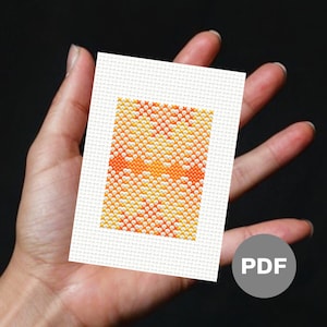 May include: A small, orange and white cross-stitch pattern on white Aida cloth. The pattern is a geometric design with a repeating motif. The cross-stitch is framed by a white border. The image includes the word "PDF" in a gray circle.