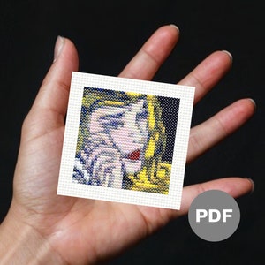 May include: A cross-stitch pattern featuring a portrait of a woman with yellow hair, blue eyes, and a red mouth. The woman is wearing a yellow and white patterned dress. The pattern is on white Aida cloth.