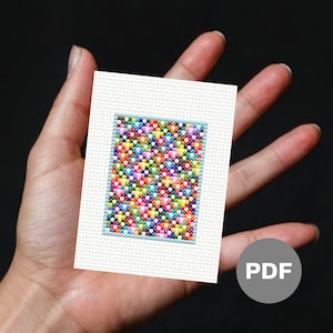 May include: A small, rectangular cross-stitch pattern with a colourful array of stitched flowers in various colours. The design is framed with a light blue border and set against a white background. A PDF icon is visible.