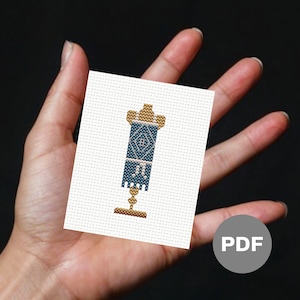Può includere: Un modello di punto croce PDF per una lampada con motivo blu e oro con frange. Il modello è su sfondo bianco.