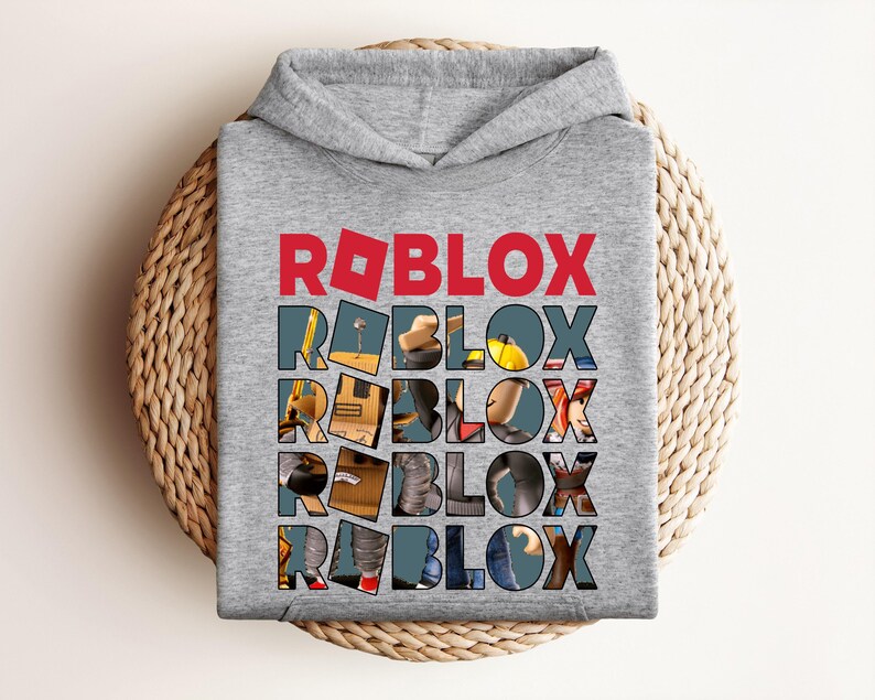 K&ouml;nnte beinhalten: Ein grauer Kapuzenpullover mit dem Wort "ROBLOX" in roten Blockbuchstaben oben. Das Wort "ROBLOX" wird f&uuml;nfmal auf der Vorderseite des Sweatshirts wiederholt, wobei jeder Buchstabe mit einem anderen Bild gef&uuml;llt ist.