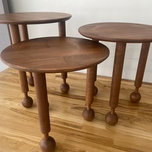 May include: Three wooden side tables with round tops and ball-shaped legs. The tables are arranged in a staggered formation, with the largest table in the back and the smallest table in the front.