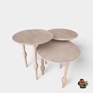 May include: Three round wooden nesting coffee tables with light wood finish and unique turned legs.