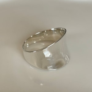 May include: A silver ring with a wide, curved band. The ring is smooth and shiny.