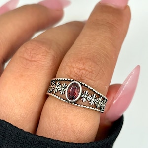 Op de afbeelding: Een zilveren ring met een rode edelsteen omringd door een delicaat bloemenmotief.