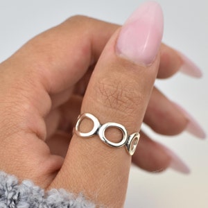 Puede incluir: Un anillo de plata con un diseño único que presenta múltiples círculos interconectados. El anillo se lleva en el pulgar.