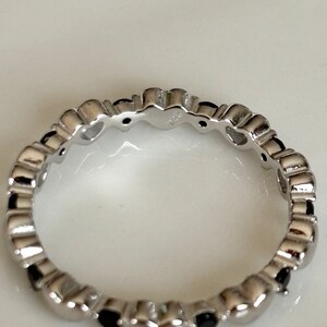 May include: A silver ring with a repeating heart design. Each heart is accented with a small, black gemstone. The ring is made of a shiny, polished metal.