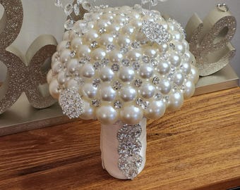 May include: A white pearl and rhinestone bridal bouquet with a white satin ribbon.