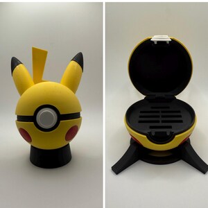 May include: A yellow Pikachu Poke Ball storage container with a black base and a black lid that opens to reveal a compartment with slots for storing game cartridges.