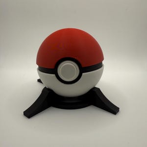 May include: A red and white Poke Ball with a black base. The Poke Ball is a popular collectible toy from the Pokemon franchise.