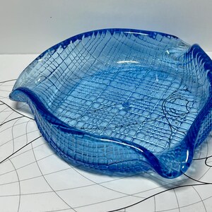 Könnte beinhalten: Eine blaue Glasschale mit einem strukturierten, gewebten Muster. Die Schale hat eine wellige, organische Form.