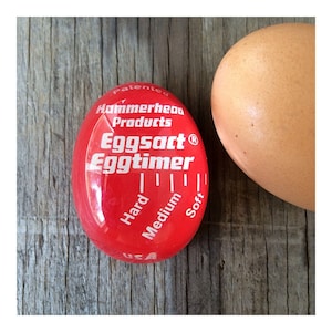 May include: A red, egg-shaped Eggtimer with the text "Eggtimer" and "Hard, Medium, Soft" indicators. Next to it is a brown egg. The Eggtimer is a kitchen gadget for cooking eggs to the desired doneness.