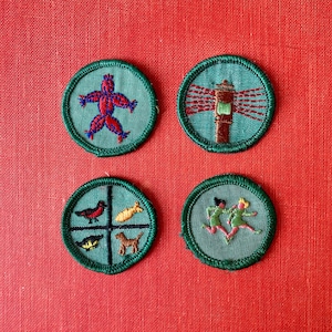 May include: Four green embroidered patches with different designs. The first patch features a red stick figure with blue details. The second patch features a white building with a red roof and a blue window. The third patch features a red bird, a yellow fish, a brown dog, and a green leaf. The fourth patch features two figures running, one in green and one in blue.