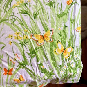 Pode incluir: Tecido branco com um padrão floral verde e amarelo com borboletas. O tecido tem um visual e uma sensação vintage.