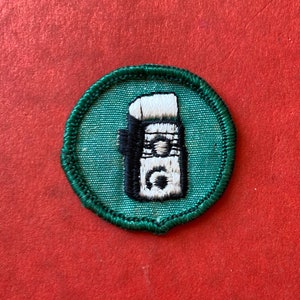 May include: A green embroidered patch with a white and black illustration of a vintage rotary phone.