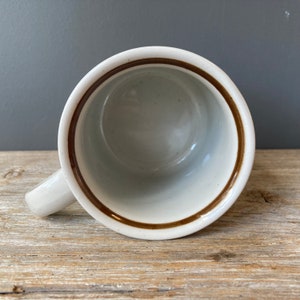 May include: White ceramic mug with a brown rim and handle. The mug is empty.