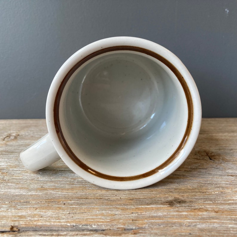 May include: White ceramic mug with a brown rim and handle. The mug is empty.