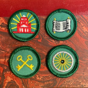 May include: Four Girl Scout badges with green backgrounds and white stitching. The badges feature a red building with yellow rays, a white scroll, two gold keys, and a white wheel with yellow spokes.