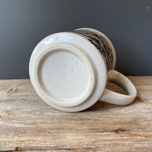 May include: White ceramic mug with a black and white design. The mug has a handle and a round bottom.