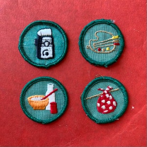 Op de afbeelding: Vier groene geborduurde badges met witte stiksels. De badges tonen een palet, een fles lotion, een kom met beslag en een rood-witte stippen tas.