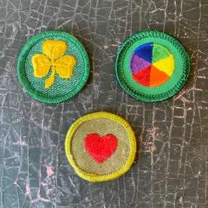 May include: Three green embroidered patches with different designs. The first patch features a yellow four-leaf clover. The second patch features a colourful pie chart. The third patch features a red heart.