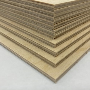 May include: A stack of thin, light-colored plywood sheets. The edges of the wood show the layered construction. The wood has a natural, unfinished appearance, with visible grain and a light tan color. The sheets are neatly stacked, suggesting a craft or construction material.