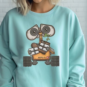 May include: A light blue sweatshirt with a graphic print of WALL-E, a robot from the animated film WALL-E, holding a plant. The robot is orange and brown with black treads.