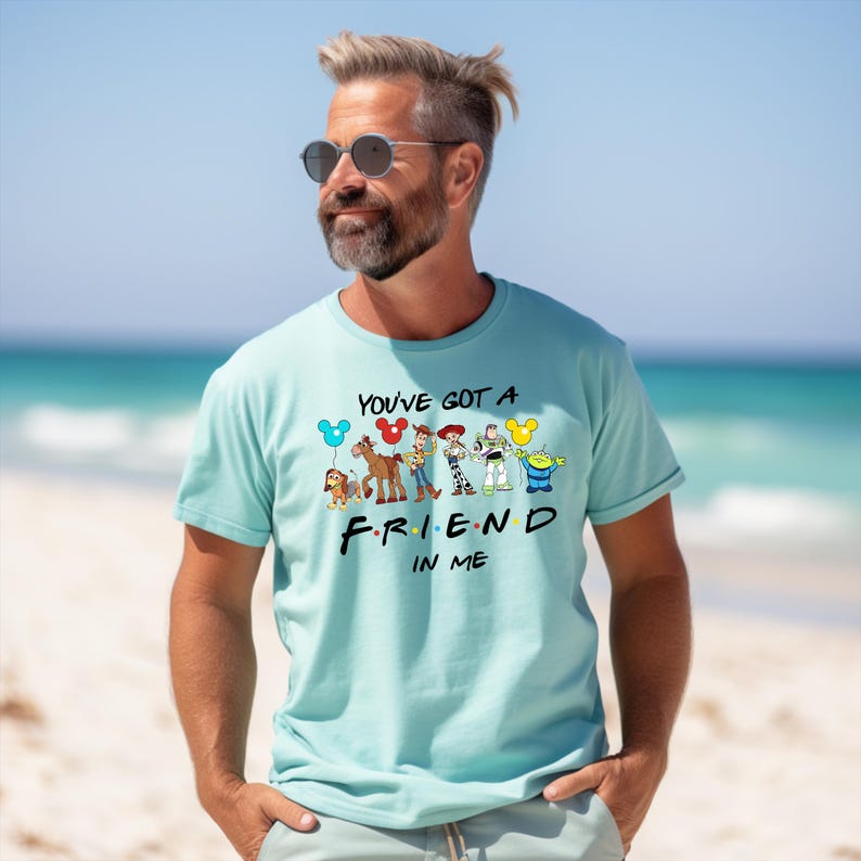 May include: A light blue t-shirt with a graphic of cartoon characters from popular animated films. The text "You've got a friend in me" is printed on the shirt.