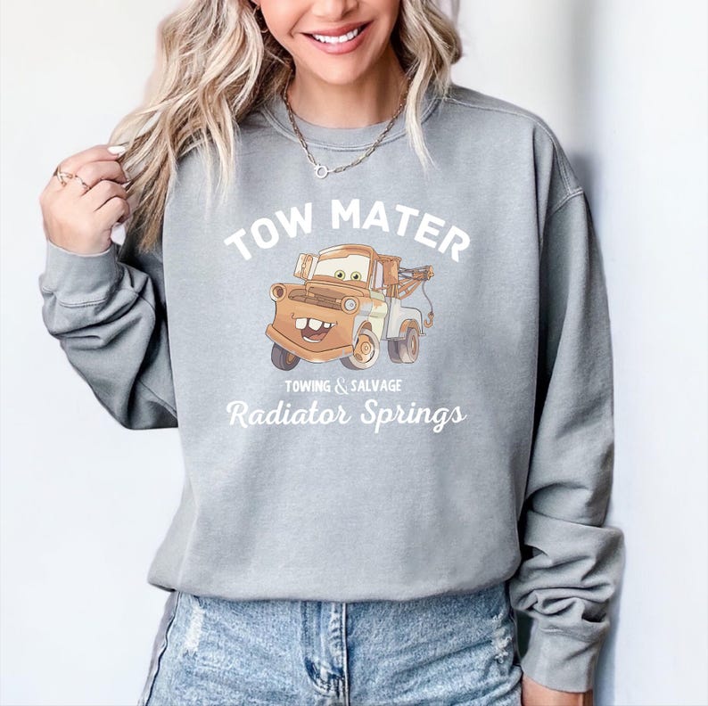 May include: Gray sweatshirt with a white graphic of Tow Mater from the movie Cars. The graphic includes the text "Tow Mater", "Towing & Salvage", and "Radiator Springs".