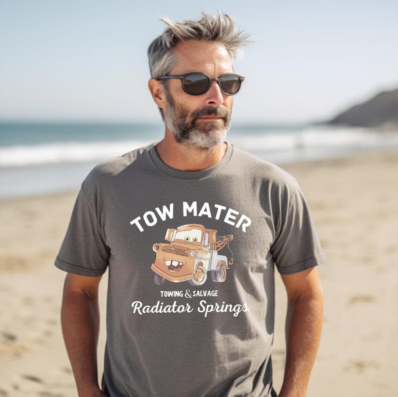 May include: A gray t-shirt with a cartoon image of Tow Mater from the movie Cars. The text on the shirt reads "Tow Mater Towing & Salvage Radiator Springs".