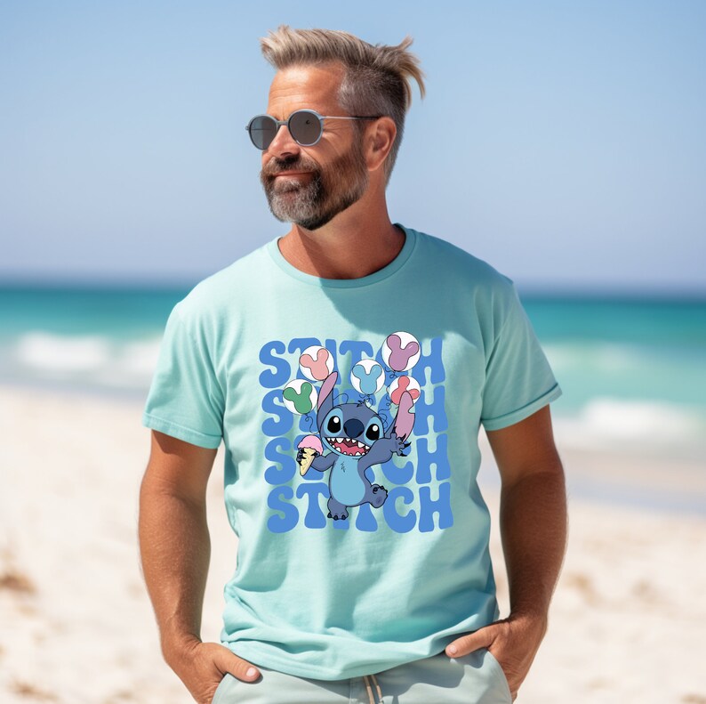 May include: A light blue t-shirt featuring the character Stitch from Lilo & Stitch. Stitch is holding ice cream and balloons. The word "STITCH" is repeated in a blue font. The shirt is short-sleeved.