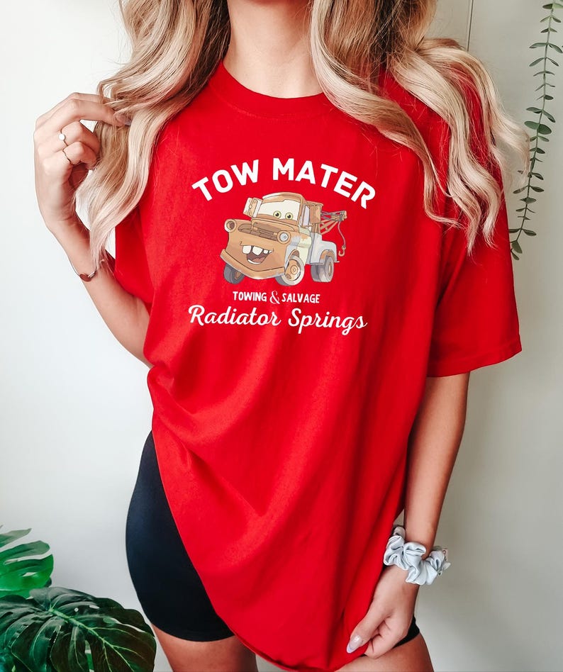 May include: Red t-shirt with a cartoon image of Tow Mater from the Cars movie. The text "Tow Mater" is printed in white above the image. Below the image, the text "Towing & Salvage Radiator Springs" is printed in white.