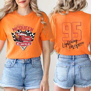 May include: Orange t-shirt with a red race car graphic and the text "Lightning McQueen Cars" on the front. The back of the shirt has the number "95" and the text "Lightning McQueen" in a cursive font.