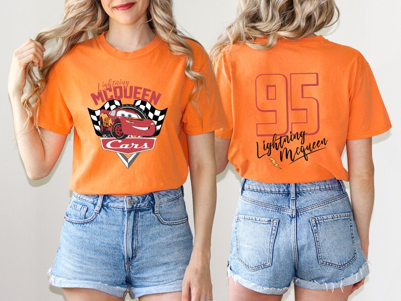 May include: Orange t-shirt with a red race car graphic and the text "Lightning McQueen Cars" on the front. The back of the shirt has the number "95" and the text "Lightning McQueen" in a cursive font.