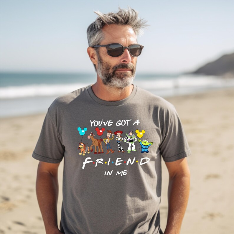 May include: A gray t-shirt with a graphic of Disney and Pixar characters, including Mickey Mouse, Woody, Buzz Lightyear, and others. The text "You've got a friend in me" is printed below the characters in a stylized font.
