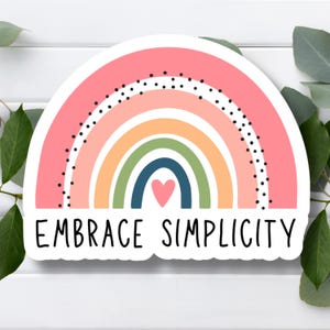 May include: A sticker with a rainbow design and the text "EMBRACE SIMPLICITY". The rainbow is made up of pink, orange, yellow, green, blue, and purple stripes. There is a small pink heart in the center of the rainbow.