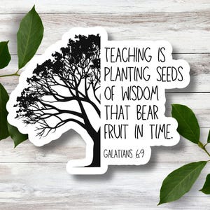 May include: A white sticker with a black tree silhouette and the text "TEACHING IS PLANTING SEEDS OF WISDOM THAT BEAR FRUIT IN TIME. GALATIANS 6:9". The sticker is on a light wood background with green leaves.