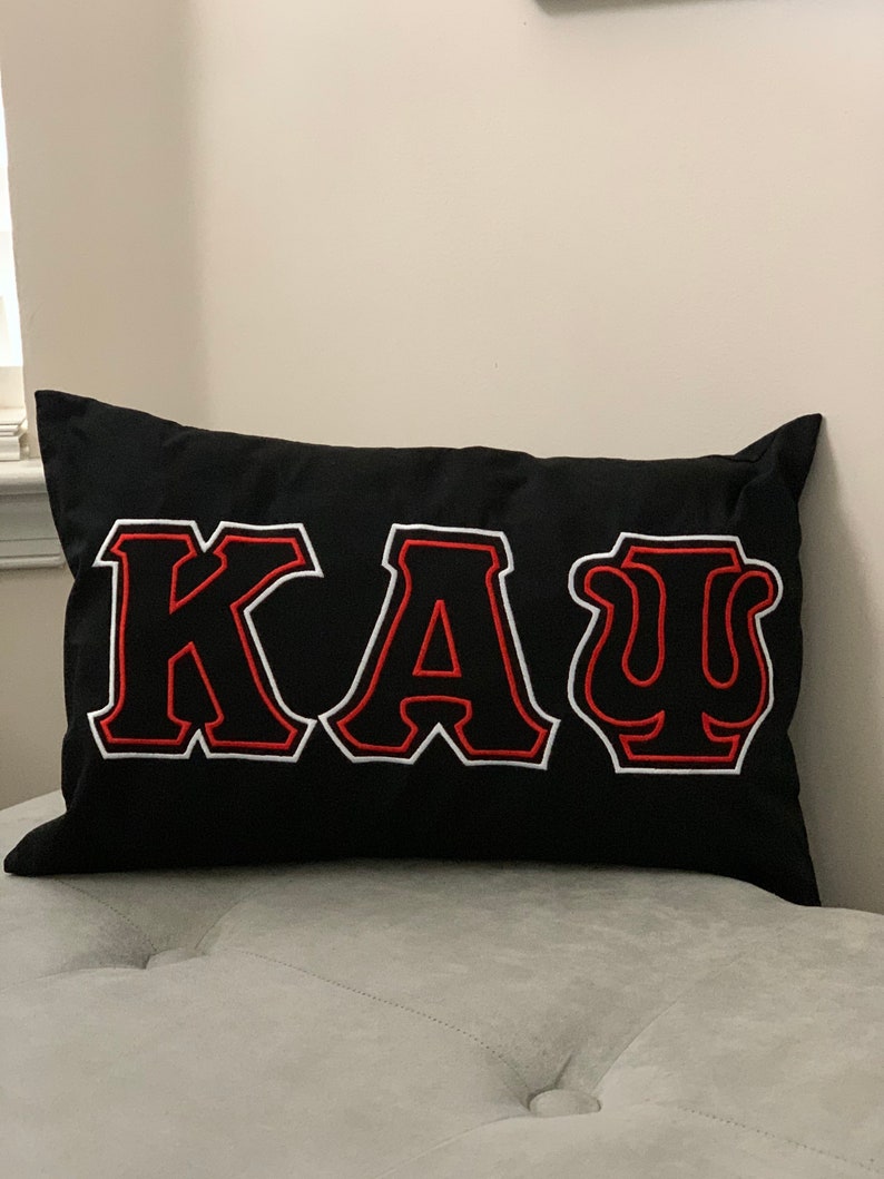 May include: Black pillow with white and red embroidered letters spelling "KAU".