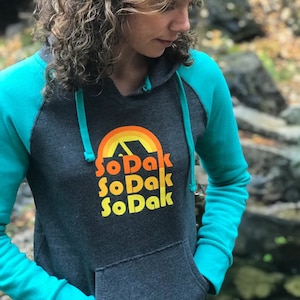 May include: A dark gray hooded sweatshirt with turquoise sleeves and a rainbow graphic with the text "SoDak SoDak SoDak" in orange and yellow.