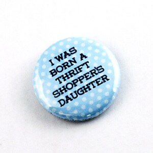 Puede incluir: Un botón azul con lunares blancos y el texto "I was born a thrift shopper's daughter".