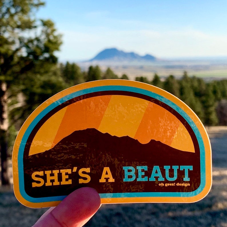 May include: A brown and yellow sticker with a mountain silhouette and the text "SHE'S A BEAUT oh geez! design".