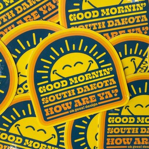 May include: A set of colorful stickers with a smiling sun and the text "Good Mornin' South Dakota How Are Ya?"  The stickers are printed on a dark blue background with yellow and orange accents.